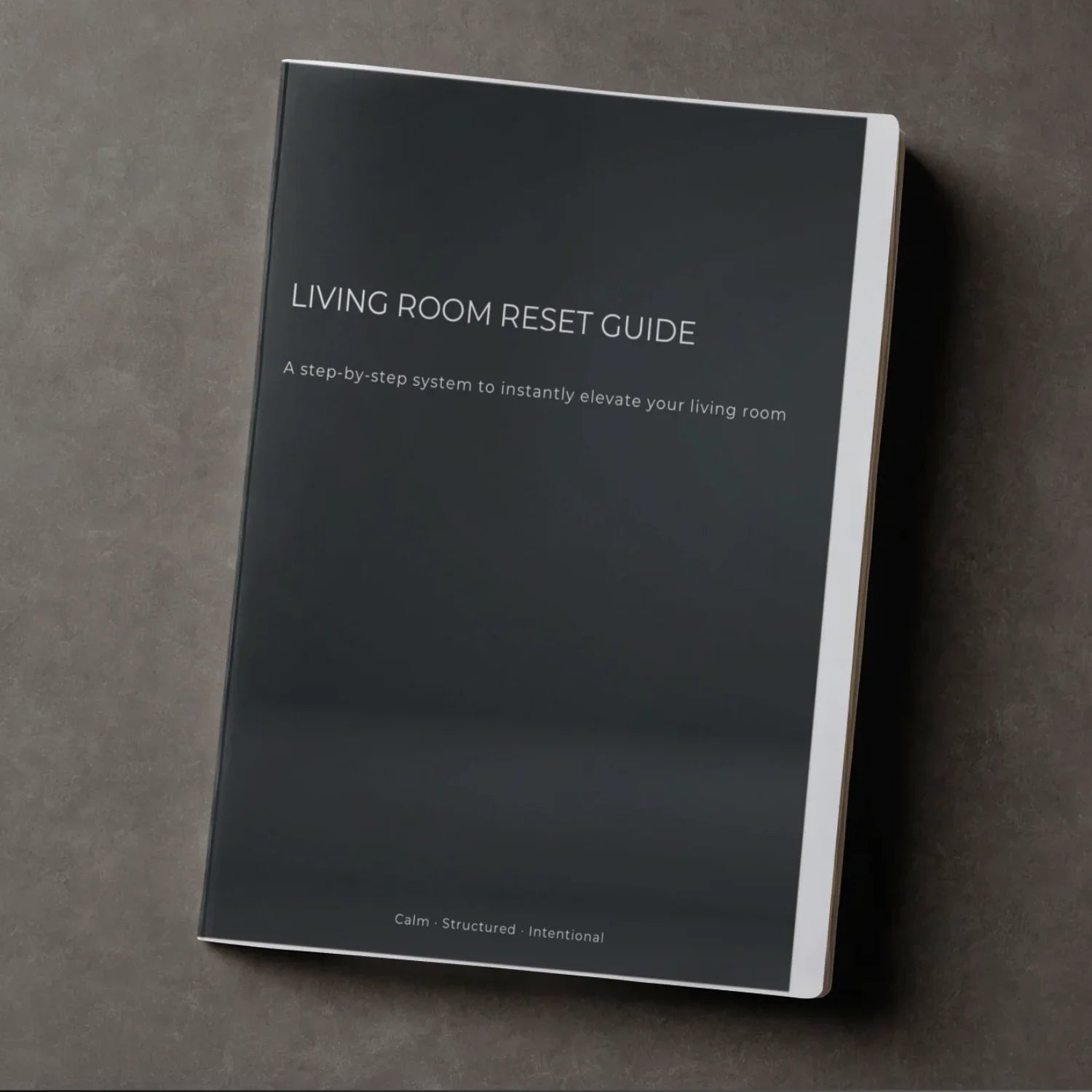 Dark cover booklet titled Living Room Reset Guide on gray textured surface